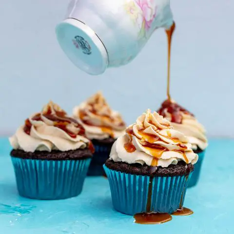drizzling caramel on top of vegan chocolate cupcakes topped with caramel buttercream frosting