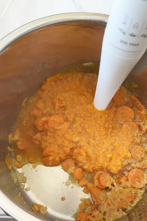blending the vegan carrot celery soup with an immersion blender.