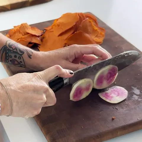 slicing a watermelon radish on a cutting board.
