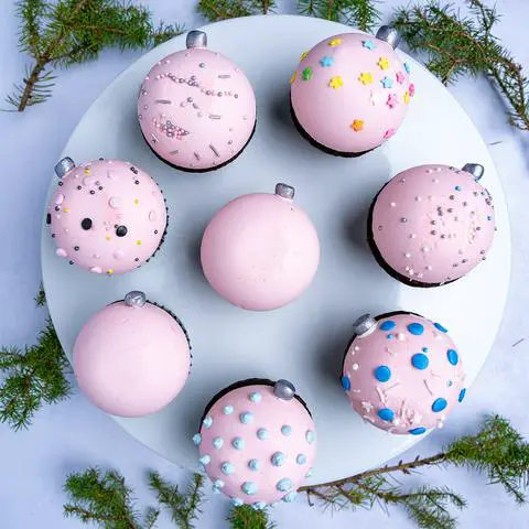 pastel pink vegan christmas ornament cupcakes on a cake stand surrounded by christmas tree branches.