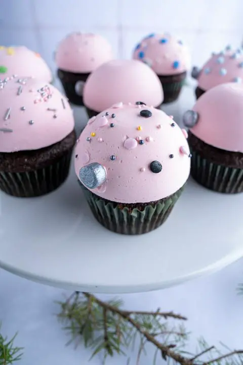 closeup of a pastel pink christmas ornament cupcake with vegan pink and black sprinkles.