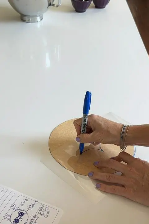 drawing the outline of the reindeer face onto the acetate to prepare for making the buttercream transfer.