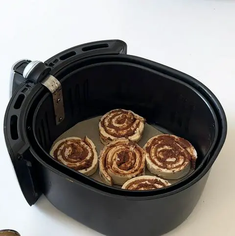 air fryer basket with 5 cinnamon rolls in it.