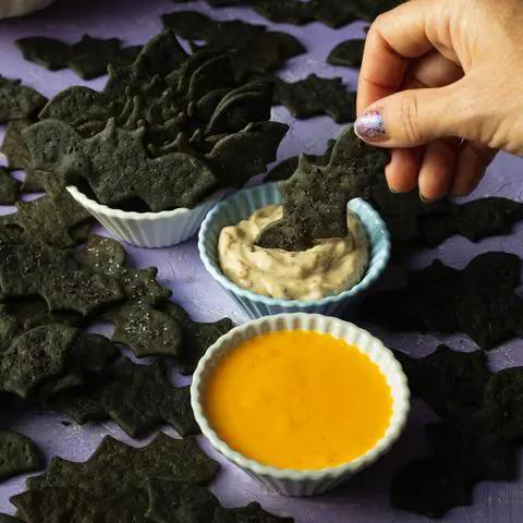 dipping a vegan black tahini bat cracker into dip.
