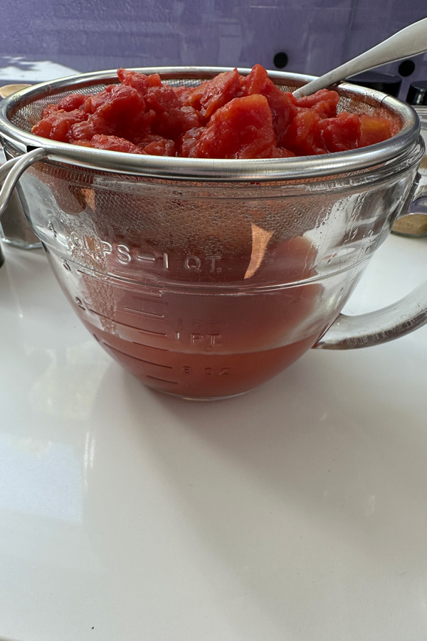 strainging the liquid from the diced tomatoes to make detroit style pizza sauce