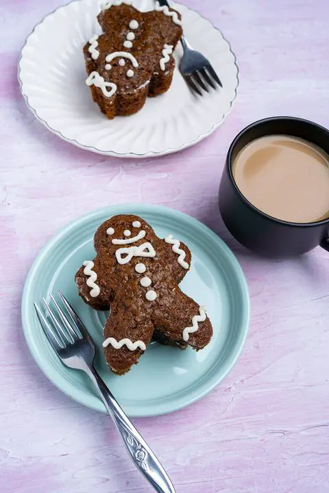 2 vegan gingerbread cakes decorated like gingerbread men next to a cup of coffee.