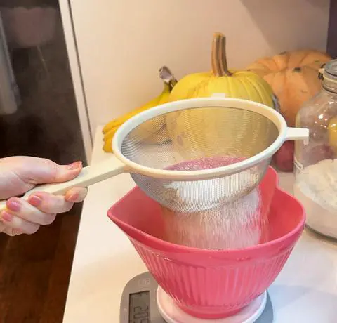 sifting the dry ingredients into a pink heart bowl.