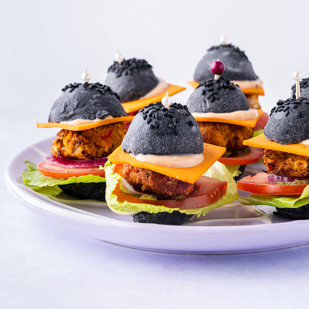 mini burgers with black buns on a plate.