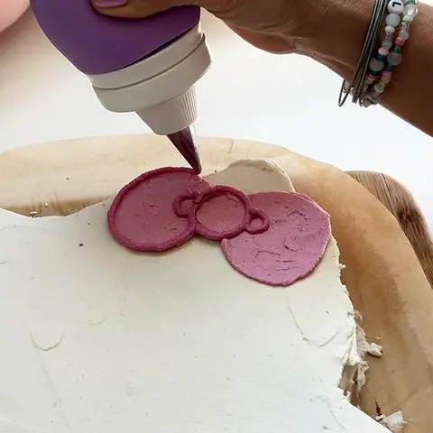 adding details to hello kitty’s bow with a frosting bulb.