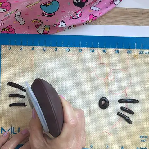 tracing the hello kitty facial features with a decopen filled with melted chocolate.