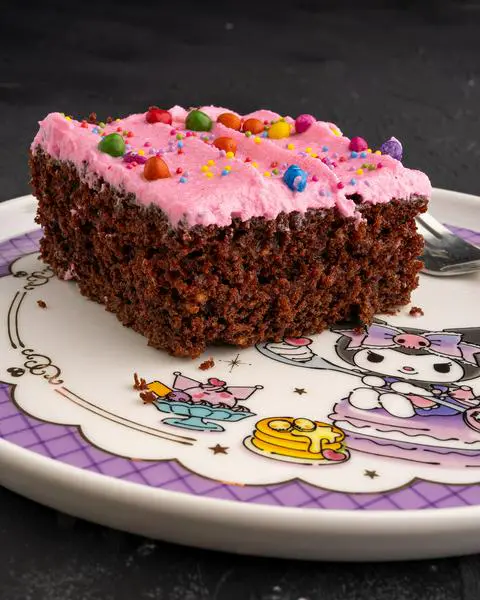 a slice of chocolate cake with pink frosting on a kuromi plate.