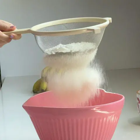 sifting the dry ingredients into a pink bowl