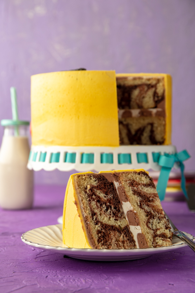 a slice of 2-layer vegan chocolate and vanilla marble cake on a plate with the rest of the pokemon cake in the background