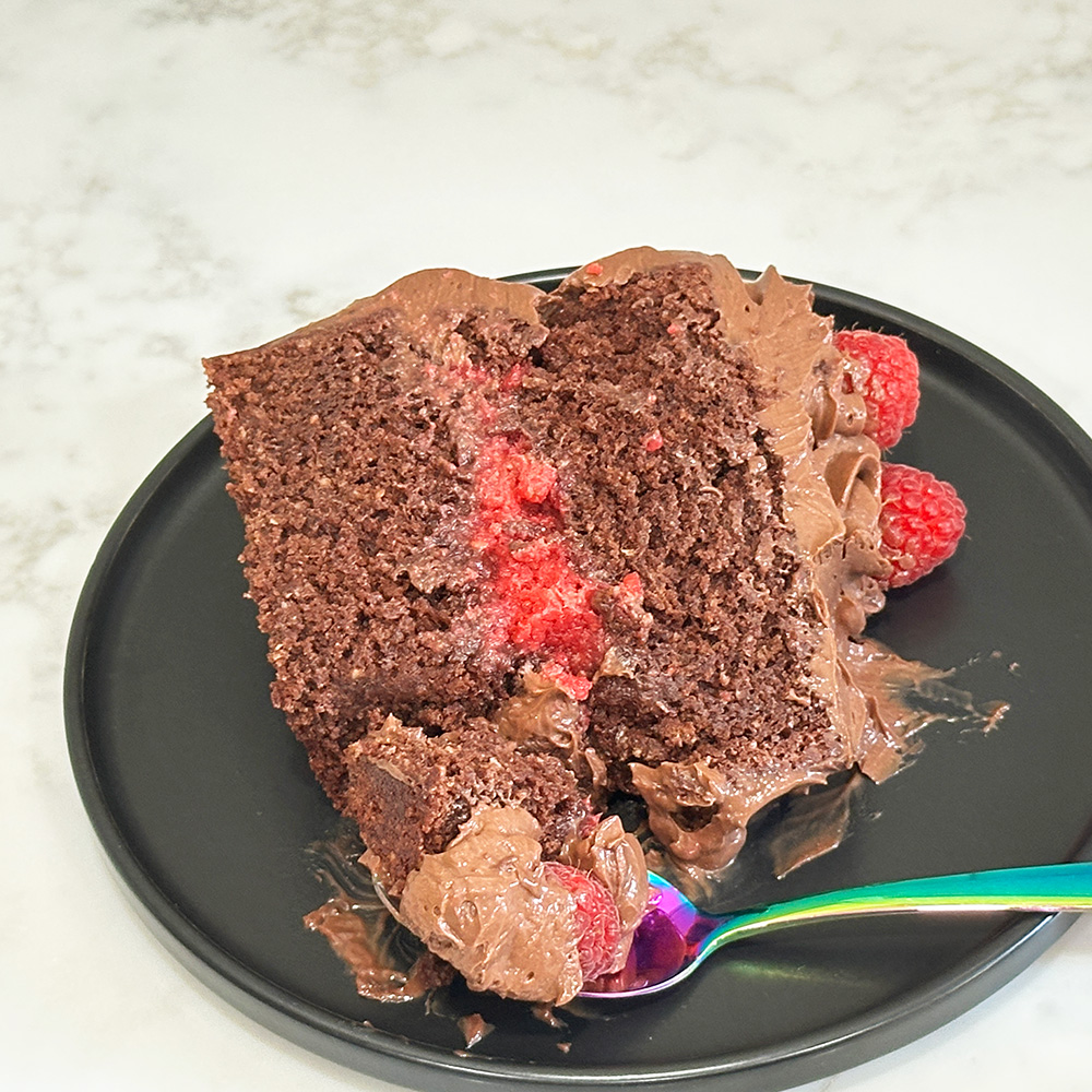 A slice of nutella raspberry cake on a plate with a bite on a spoon.