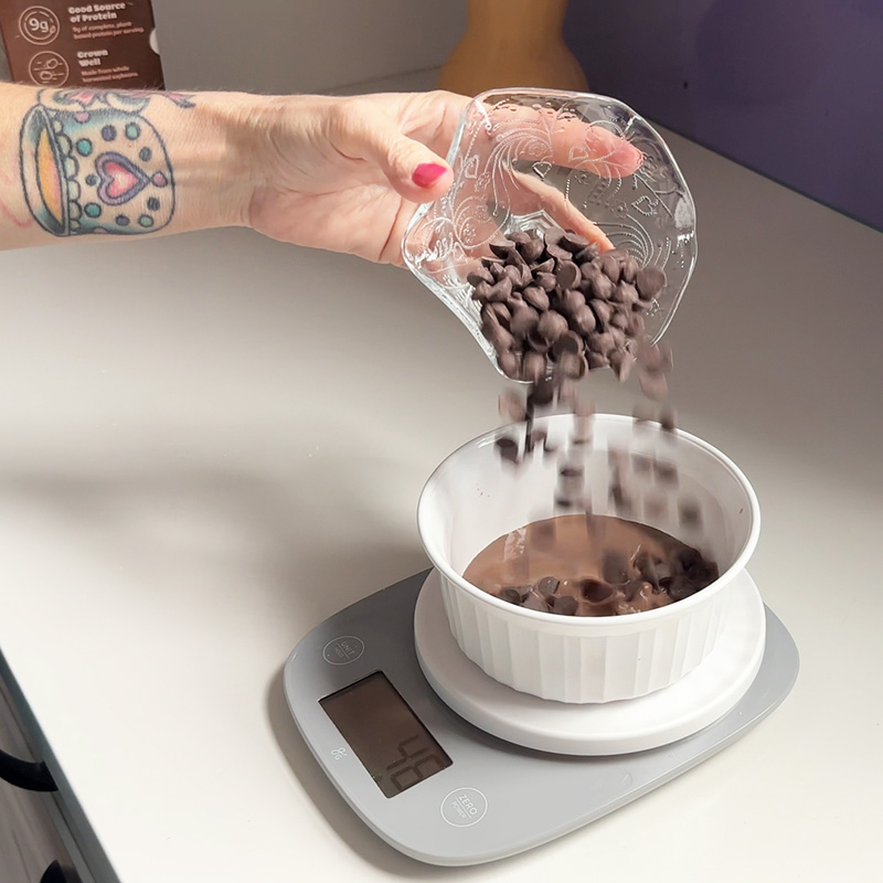 Pouring chocolate chips into a bowl with chocolate soymilk.