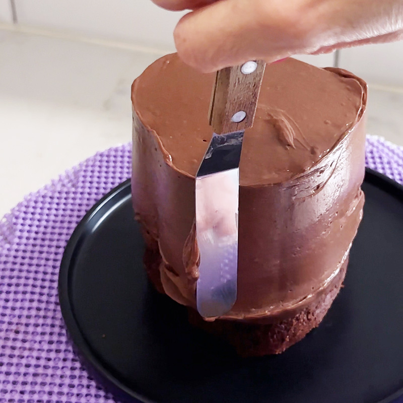 Using a mini offset spatula to smooth out the sides of the 4-inch raspberry nutella heart cake.