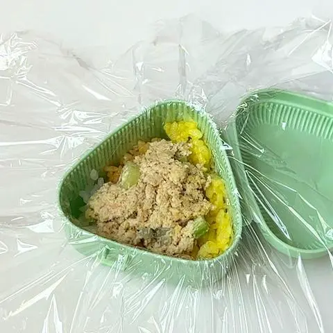 onigiri mold with cling wrap, the bottom layer of rice, and the tuna filling layer.