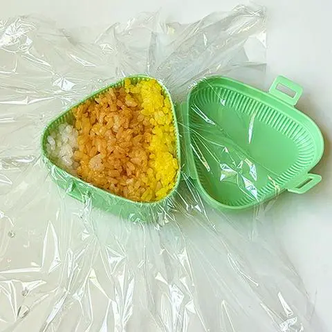 onigiri mold with cling wrap, the bottom layer of rice, the tuna filling layer, and the top layer of rice.