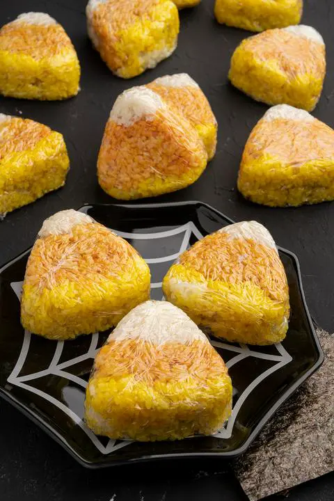 3 tuna onigiri on a black spider web plate with more onigiri on a black table around the plate.