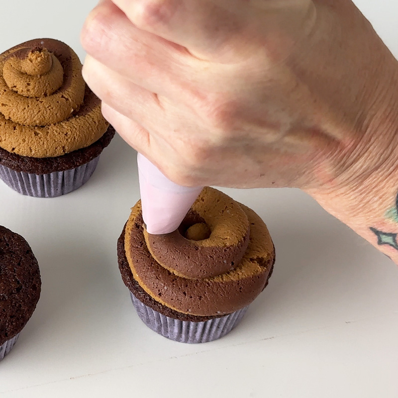 piping a swirl of vegan chocolate and peanut butter frosting on a gluten-free cupcake.