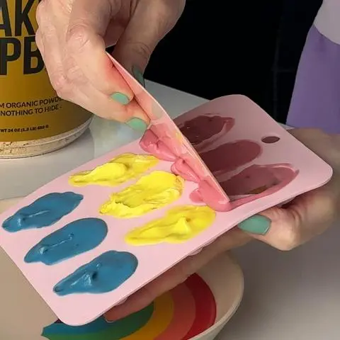 scraping excess chocolate off the top with a pink scraper.