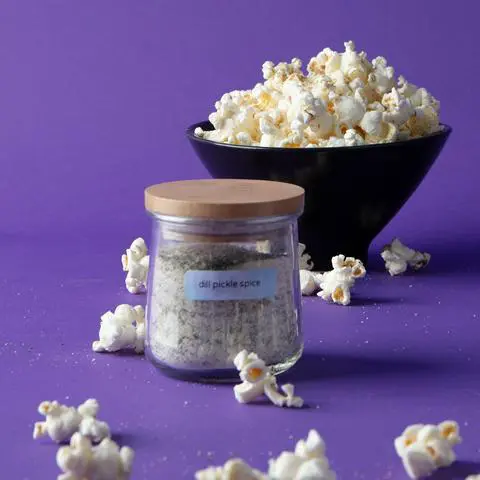 a jar of dill pickle seasoning surrounded by dill pickle popcorn.