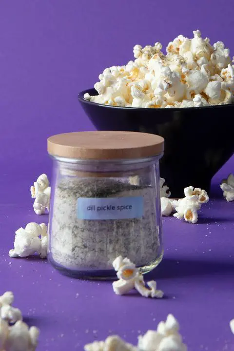 a jar of dill pickle seasoning surrounded by dill pickle popcorn.