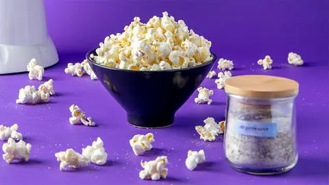 a bowl of dill pickle popcorn with popcorn on the table, and dill pickle seasoning in a jar.
