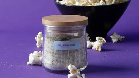 a jar of dill pickle seasoning surrounded by dill pickle popcorn.