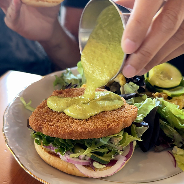 pouring sauce onto a vegan chicken sandwich at June in Portland.