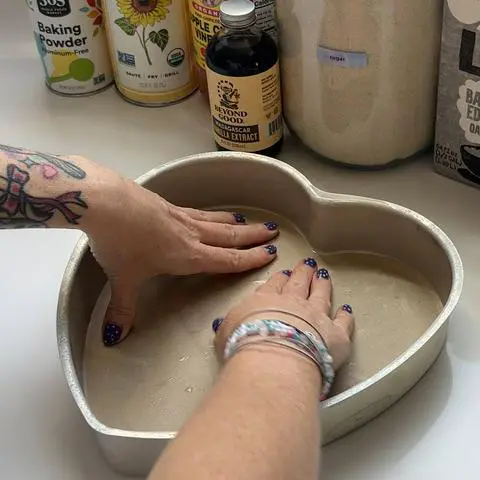 using both hands to smooth the heart shaped piece of parchment paper into the bottom of the cake pan.